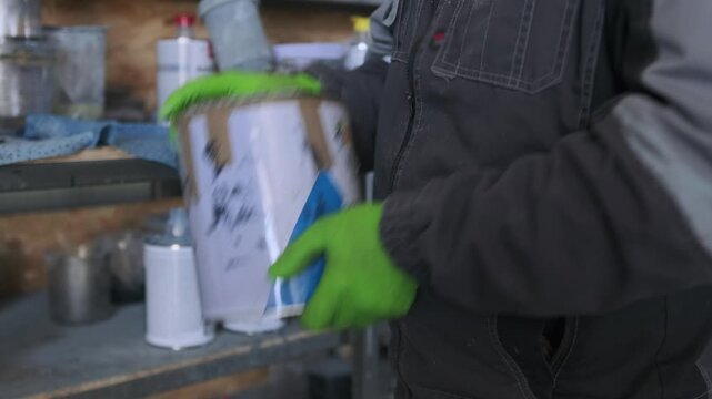 Auto body technician shaking automotive paint container before mixing materials and preparing spray equipment for vehicle repainting in professional workshop.