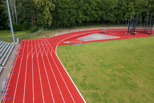 Aerial view of red running track and green athletic field surrounded by lush trees and stadium seating Vilnius County, Lithuania.