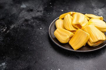 Sweet, golden yellow jackfruit pods (bulbs) served in a black plate on a dark stone background. Exotic tropical fruit with copy space © Mironov