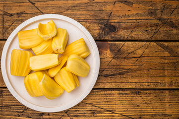 Sweet, golden yellow jackfruit pods (bulbs) served on a white plate on a rustic wooden table. Fresh, tropical fruit snack. © Mironov