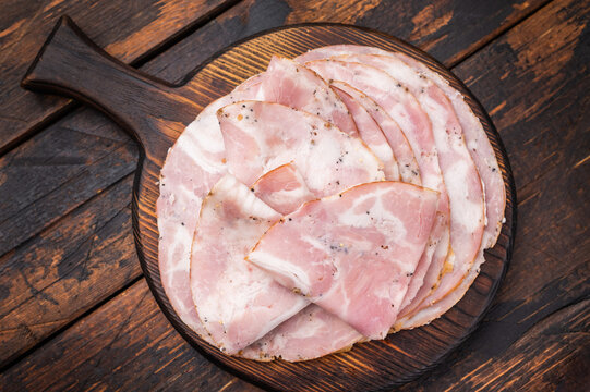 Slices of authentic Italian Pancetta Arrotolata served on a dark rustic cutting board with fresh thyme and peppercorns.