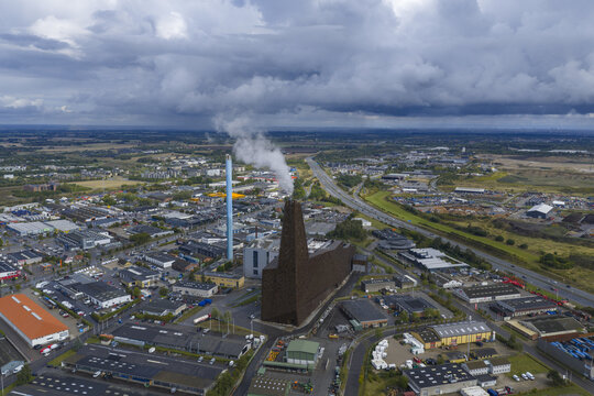 Aerial view of Energitarnet waste-to-energy plant with steam rising from the chimney and surrounding industrial buildings under heavy clouds Roskilde, Denmark.