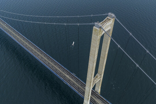 Aerial view of the Great Belt Bridge pylon and suspension cables over the dark blue sea with a small sailboat below Denmark.