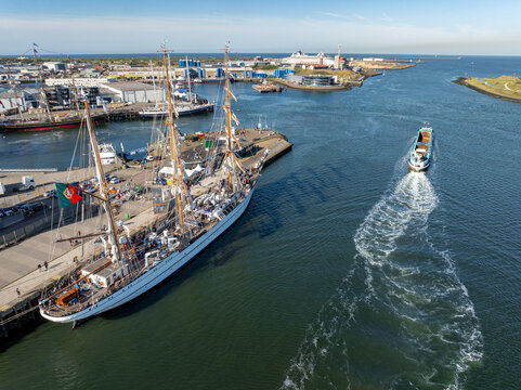 Velsen, Netherlands - 19 August 2025: Aerial view of a large Portuguese sailing ship, NRP Sagres, docked at the harbor with industrial buildings and a moving boat in the background.