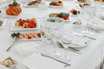 Fototapeta premium Close-up of a formal place setting with clear wine glasses, a white folded napkin, and plates of fresh appetizers on a banquet table.