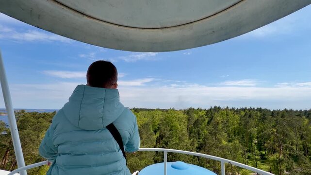 Back view of boy looking at forest and sea horizon from the top of ferris wheel at high altitude