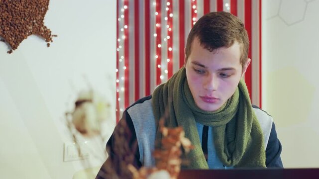 Caucasian man contemplative beside laptop, sipping cup red curtain and fairy lights create warm bokeh, dried flowers in foreground, green scarf, pensive gaze, latenight creative editing, quiet
