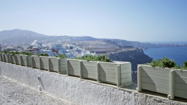 Santorini terrace with planter boxes and whitewashed stone walkway, distant caldera village rendered soft and defocused bokeh street; backplate template overlay calm.