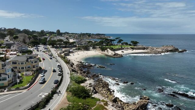 Cinematic aerial drone footage of Lovers Point Park in Pacific Grove, California, showcasing rocky coastline, turquoise ocean water, sandy beach cove, scenic coastal road, oceanfront homes, Monterey