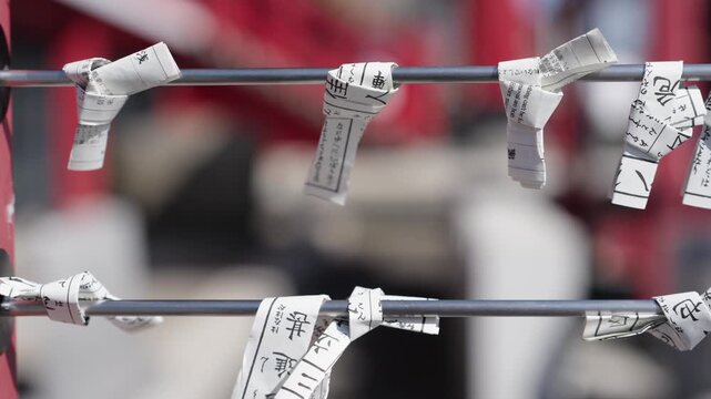 Rolled omikuji fortune papers with kanji tied to metal rods at shrine with blurred crowd background Japan