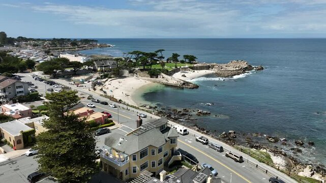 Cinematic aerial drone footage flying forward above Pacific Grove, California, toward Lovers Point Park, showcasing turquoise Pacific Ocean water, rocky shoreline, coastal walking paths, oceanfront