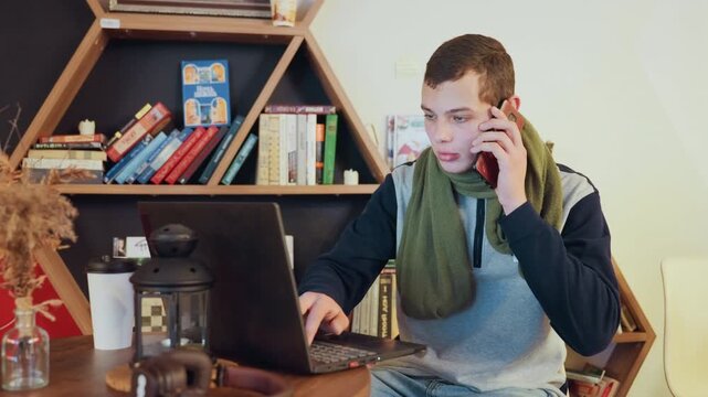 White man tutoring online via laptop and phone in warm study, gesturing while explaining, cup of coffee nearby, hexagonal bookshelf backdrop, focused instructor delivering remote lesson