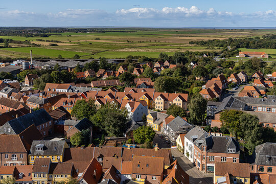 View of the historic red-tiled rooftops and surrounding green fields from Ribe Cathedral under a blue sky in Ribe, Denmark.