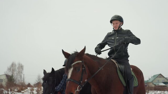 Caucasian ranger on chestnut horse surveying horizon winter patrol posture steady reins in hand helmet leather jacket silhouette against overcast sky attentive gaze control over mount close village