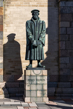 View of the bronze statue of Hans Tausen holding a book in front of a brick wall at Ribe Cathedral Ribe, Denmark.