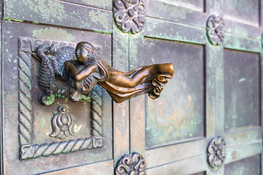 View of the ornate bronze door handle featuring a sculpted figure on the weathered green metal doors of Ribe Cathedral in Ribe, Denmark.