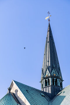 View of historic Ribe Cathedral spire featuring a golden weather vane and oxidized green copper roof against a clear blue sky with a small bird Ribe, Denmark.