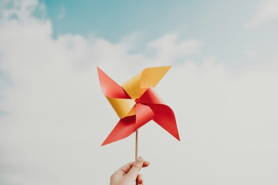 A hand holds a colorful pinwheel under a cloudy sky outdoors.