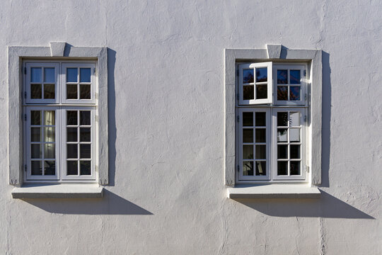 View of two white-framed windows on a textured facade with sharp shadows in Ribe, Denmark.