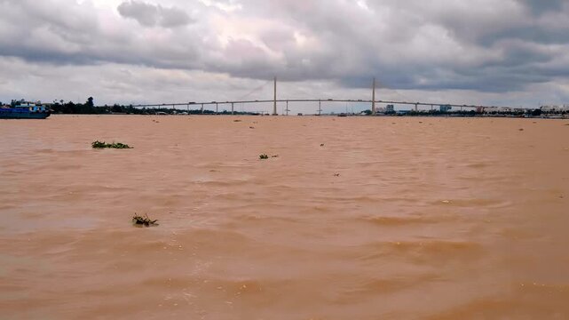 The cable-stayed Rach Mieu Bridge in Vietnam connecting Tien Giang Province and Ben Tre Province spans above yellow sandy muddy waters of Mekong River under the picturesque cloudy sky
