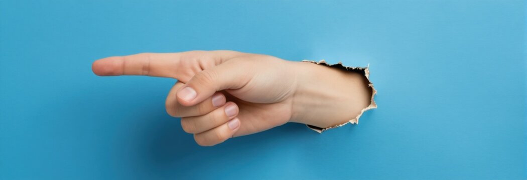 Hand points to the right through a torn hole in a blue paper background. Index finger extended shows direction or indicates something important. Copy space available.