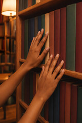 Obraz premium Dark Skin Woman Hands Touching Colorful Book Spines on Warm Library Shelf