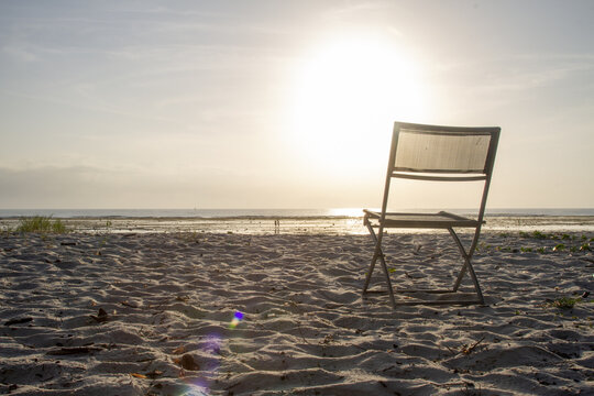View of Tiwi Beach with a lone folding chair on the sandy shore facing the bright sun over the ocean horizon at sunrise Tiwi, Wilaya ya Kwale, Kenya.
