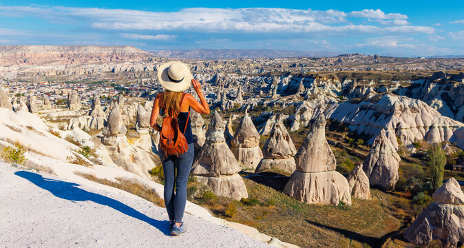 Young woman traveler with backpack and straw hat looking at Cappadocia fairy chimneys landscape in Turkey