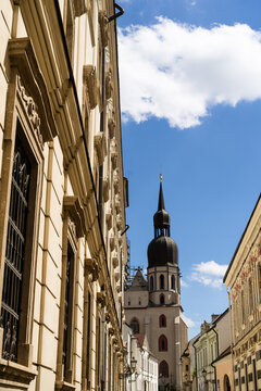 View of the historic St. Nicholas Basilica tower rising above narrow streets and ornate facades under a blue sky in Trnava, Trnava Region, Slovakia.