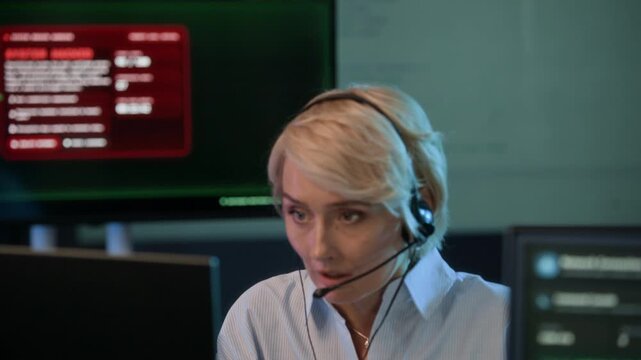 Handheld shot of adult Caucasian female coordinator monitoring cyberattack and reporting threat using headset in cybersecurity office