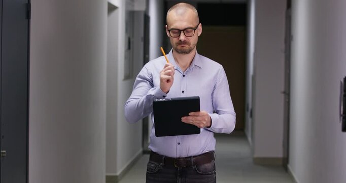 Businessman stands in corridor and writes detailed notes in official document. Serious man with clipboard conducts thorough inspection of modern residential building