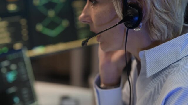 Tilt up close up shot of adult Caucasian cybersecurity operator wearing headset monitoring digital network interface and system data in control room and providing technical support