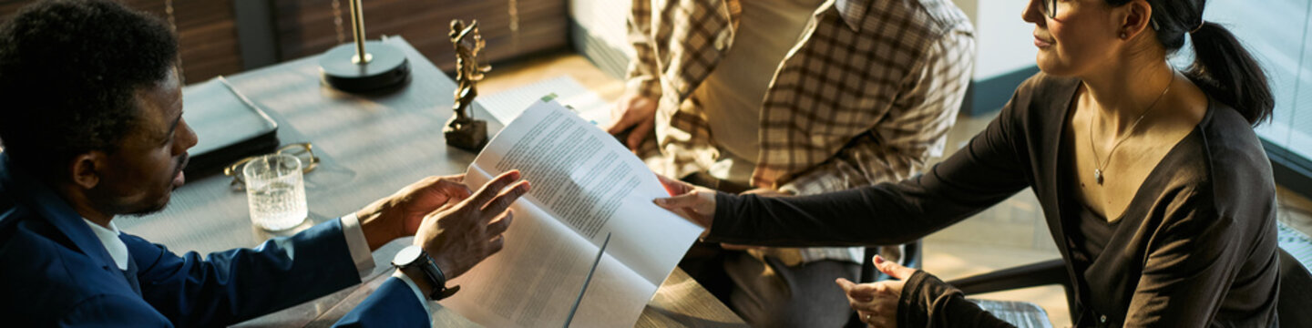 Wide angle view of middle aged couple meeting lawyer, reviewing divorce papers and discussing legal separation during consultation. Ideal for family law, mediation, custody marketing