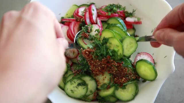 Close-up of preparing a simple summer salad by tossing sliced cucumbers and radishes with mustard dressing in a large salad bowl