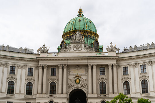 View of the ornate facade and green dome of the Hofburg Palace with baroque sculptures and classical columns under an overcast sky Vienna, Vienna, Austria.
