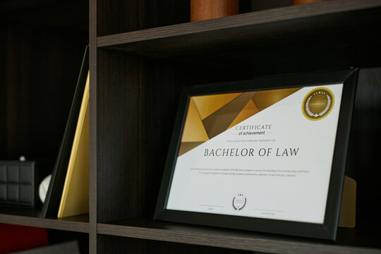 Close up of framed Bachelor of Law certificate standing on shelf, representing legal qualification, attorney career path, divorce law expertise. Useful for legal service marketing