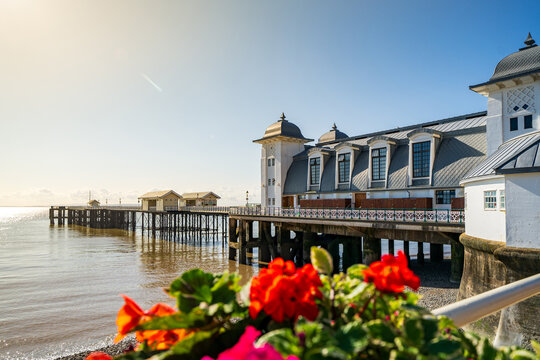 View of the historic Penarth Pier Pavilion with its Victorian architecture and red flowers in the foreground under a clear sky in Penarth, United Kingdom.