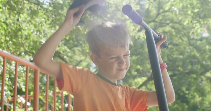Boy holds tall scooter handle looking forward with bright smile in park. Child steadies orange ride with right hand preparing to move again after short riding pause