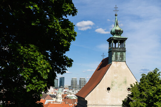 View of the historic Franciscan Church tower with a green copper spire and the modern Sky Park skyscrapers in the background in Bratislava, Bratislava Region, Slovakia.