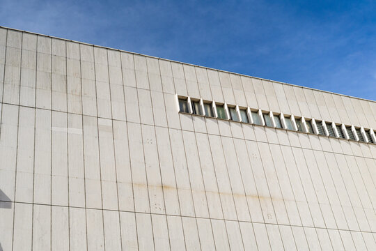 View of the minimalist white facade of a modern building with vertical stone panels and a row of narrow windows under a clear blue sky in Bratislava, Bratislava Region, Slovakia.