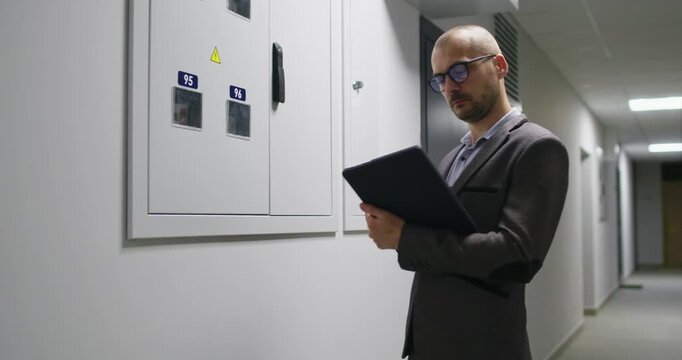 Businessman inspects digital counter and accurately transfers readings into detailed document. Attentive man in glasses records meter values into official documentation