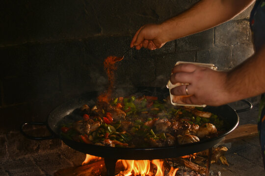 Man seasoning traditional Valencian paella in wood fired oven