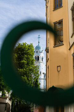 View of the Blue Church with its distinctive light blue tower and facade framed through a circular green element in Bratislava, Bratislava Region, Slovakia.