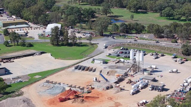 Drone aerial view of a concrete batching plant and industrial yard near Wodonga, Australia. Cement silos, aggregate stockpiles, trucks and surrounding green countryside visible 
