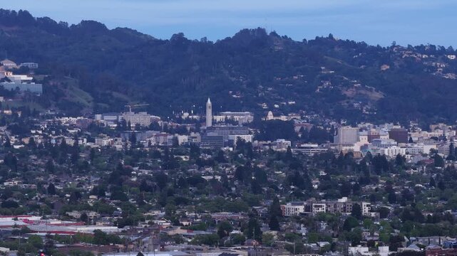 Scenic aerial view of the Berkeley cityscape with the iconic Sather Tower, also known as the Campanile, surrounded by dense trees and the Berkeley hills during a tranquil evening