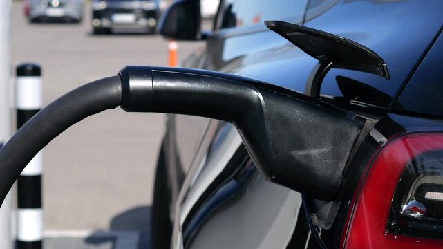 Close up of a black electric car plugged into a charger at a public station, showcasing sustainable automotive technology and the future of clean energy transportation for modern mobility
