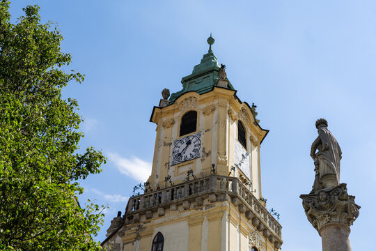 View of the historic Old Town Hall clock tower and the Maximilian Fountain statue under a clear blue sky in Bratislava, Bratislava Region, Slovakia.