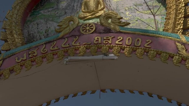 Close up of the ornate temple arch on Don Khon Buddhist Temple, Laos, showing gold trim, a seated Buddha figure and decorative carvings.