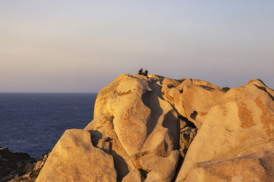 View of Capo Testa granite rock formations with two people sitting on the summit overlooking the Mediterranean Sea during golden hour Capo Testa, Sardegna, Italy.