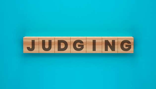 Judging Word Blocks: A close-up shot of the word JUDGING spelled out with wooden blocks set against a vibrant turquoise backdrop. This image embodies the concept of assessment, evaluation.